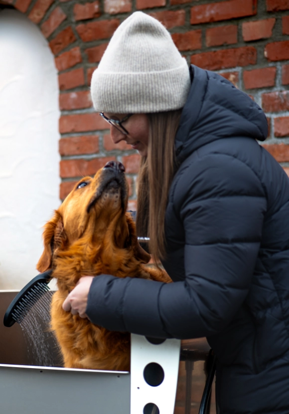 Frau wäscht Hund in Hundedusche